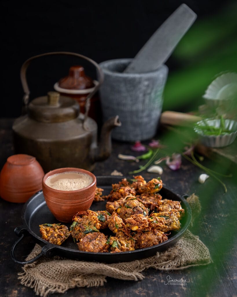 Crispy Raw Jackfruit Chana Dal Fritters (Panasa Buta Dali Bara) served with a cup of tea in a rustic traditional setting.